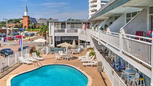 Hotel med swimmingpool, liggestole og udsigt til en kirke og bygninger i baggrunden.