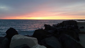 A beach with large rocks in the foreground and a sunset in the background. - Sea Fly Guest House (Fiumicino)