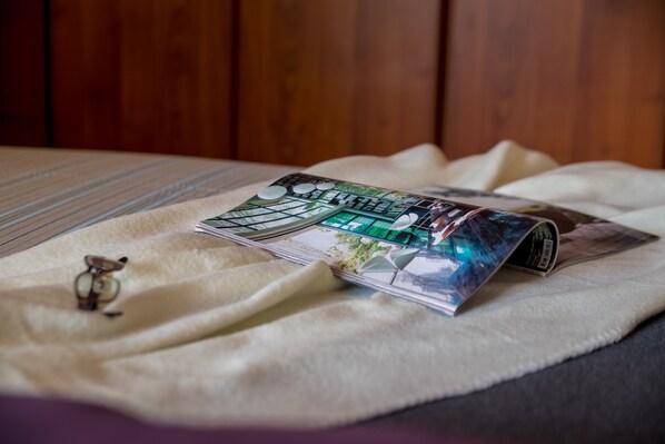 A magazine on a bed with a striped blanket and a pair of glasses.