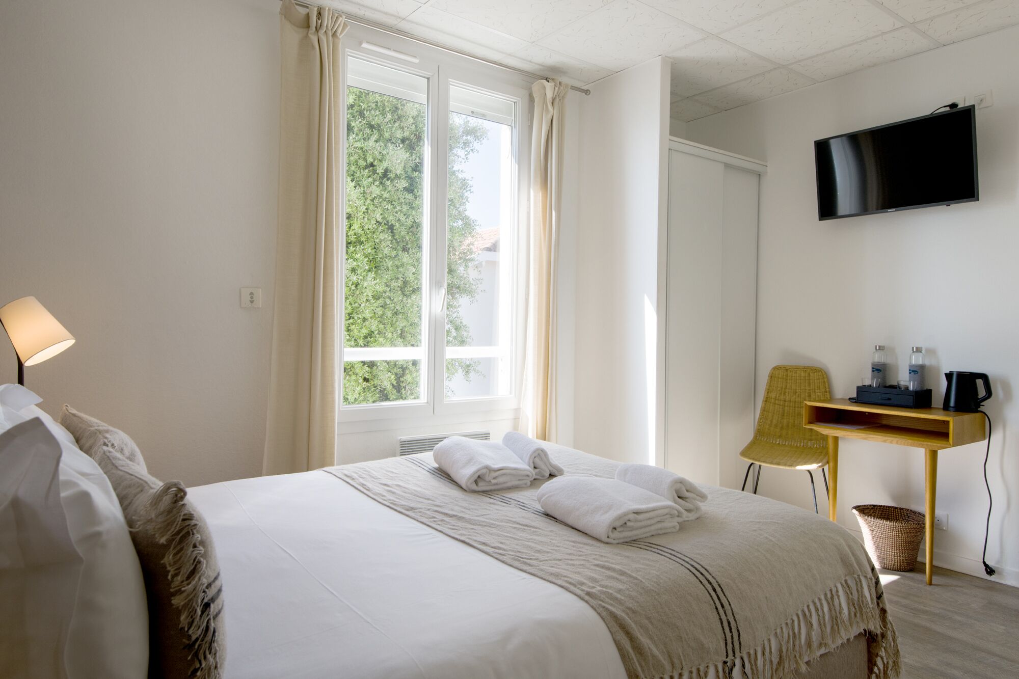 A hotel room with a bed, a desk, a chair, a TV, and a window with curtains.