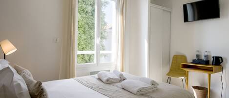 A hotel room with a bed, a desk, a chair, a TV, and a window with curtains.