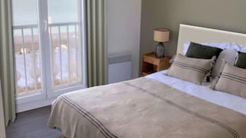 Une chambre à coucher avec un lit, une table de chevet, une lampe et une vue sur la plage, accessible par une porte coulissante.