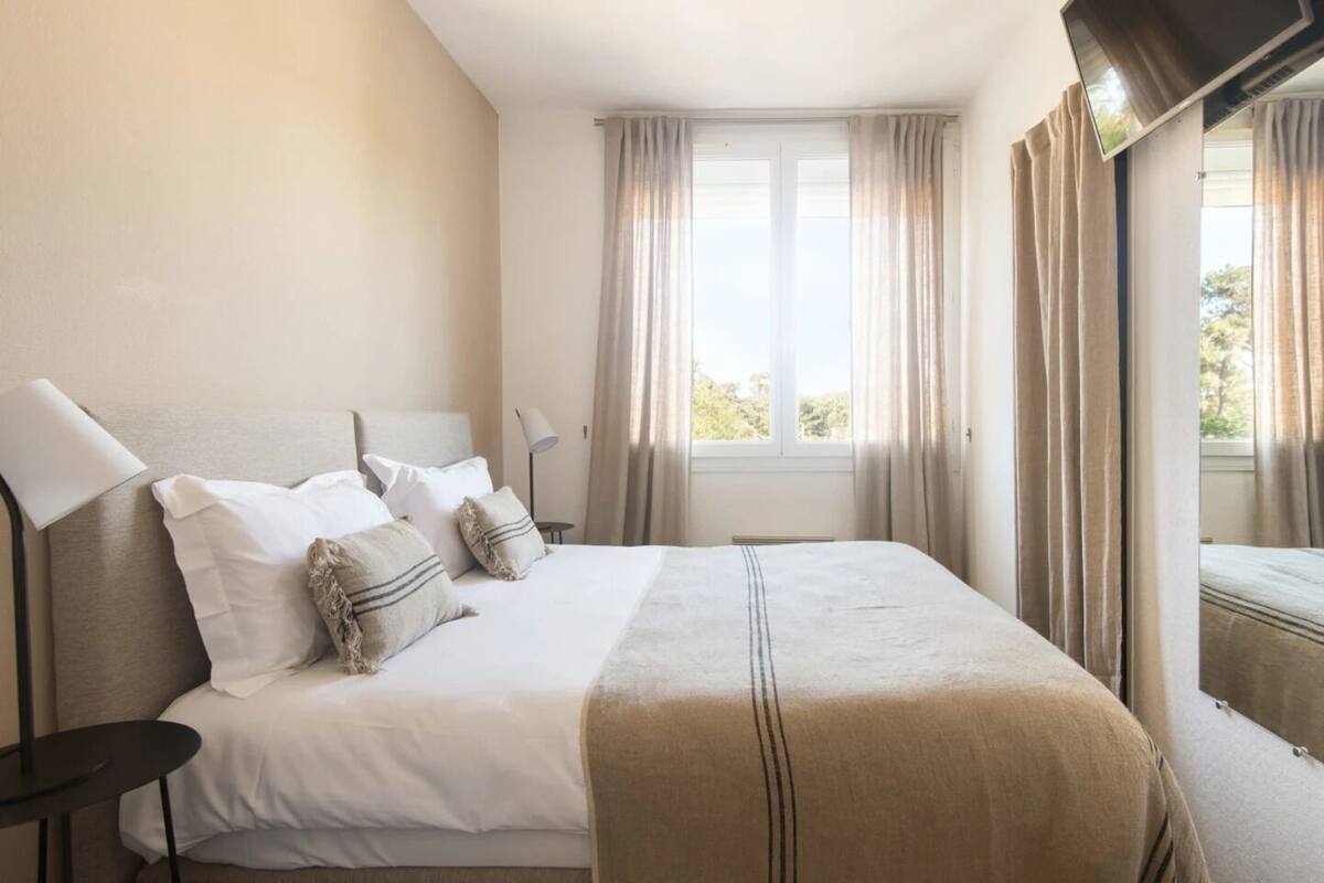 A neatly made bed with a headboard, a bedside lamp, and a window with curtains.