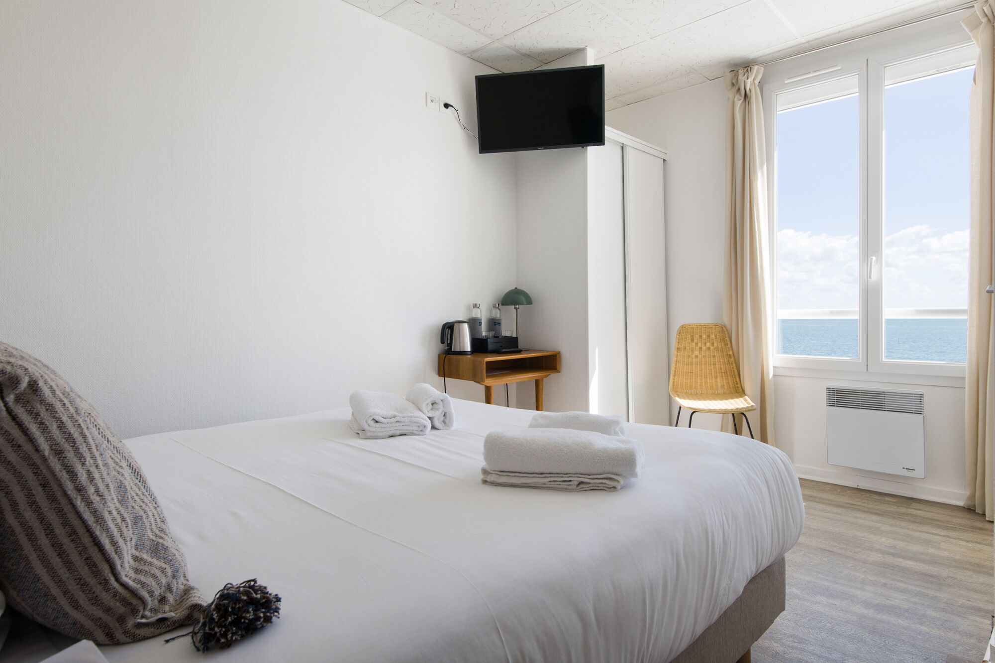 Une chambre d’hôtel avec un lit, un bureau avec une lampe, une chaise et un téléviseur fixé au mur.