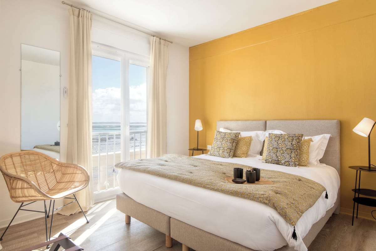 A bedroom with a bed, bedside lamps, a chair, and a view of the outdoors.