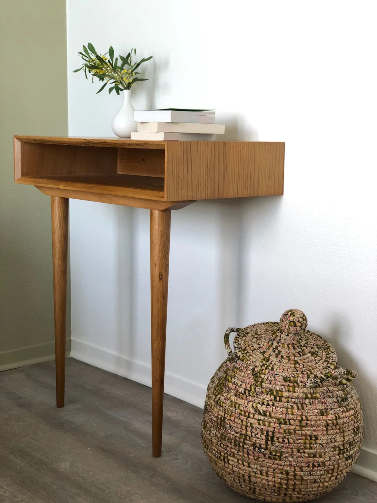 A wooden console table with a white vase and books, next to a woven basket.