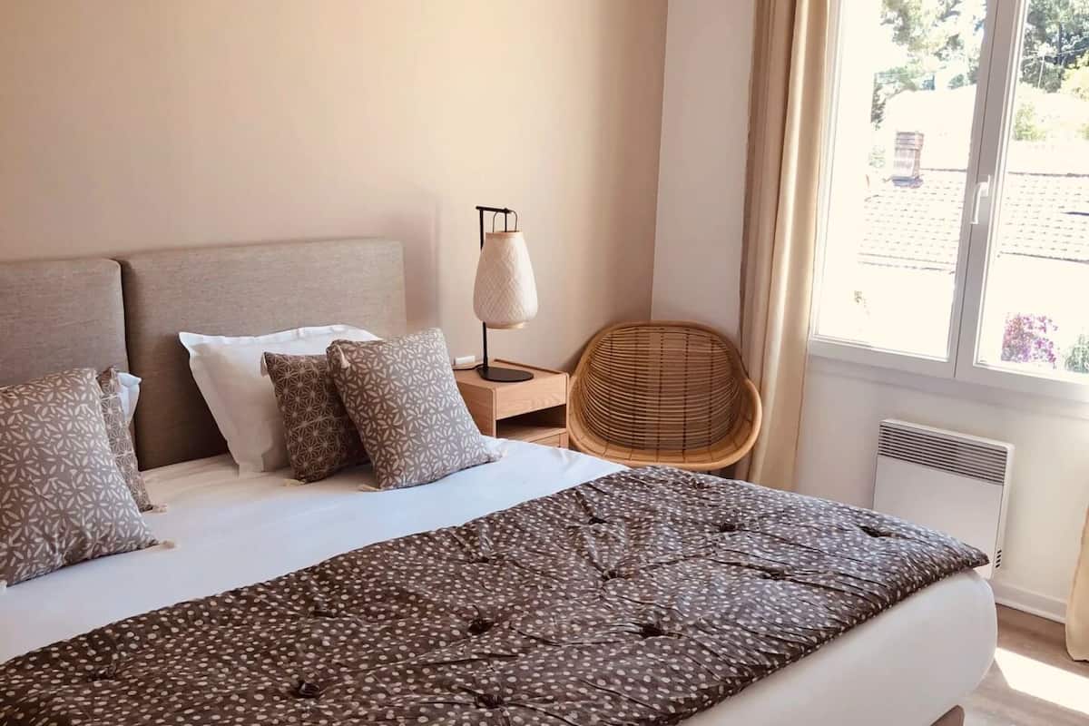 A neatly made bed with a polka dot duvet, a bedside lamp, and a wicker chair.
