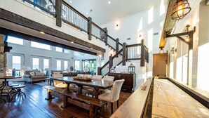A spacious loft-style living area with a high ceiling, wooden flooring, and a large dining table. - Breathtaking Views, Hot Tub (Broken Bow)