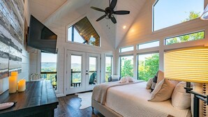 A bedroom with a large bed, a desk with candles, a ceiling fan, and a view of the outdoors. - Breathtaking Views, Hot Tub (Broken Bow)