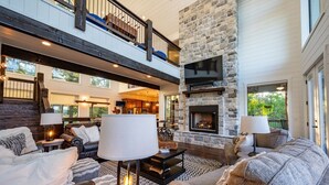 A spacious living room with a stone fireplace, leather sofas, and a high ceiling with exposed beams. - Breathtaking Views, Hot Tub (Broken Bow)