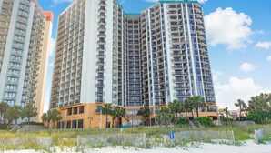 Un hotel moderno de gran altura con varios balcones, vista a la playa y arena en primer plano.