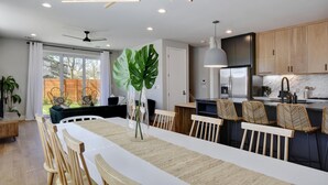 Una cocina moderna con armarios de madera, encimera blanca y un comedor con una mesa larga y sillas.