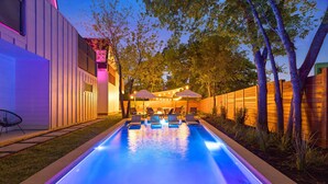 Piscina con sillas de descanso y sombrillas, rodeada por una valla de madera y árboles.
