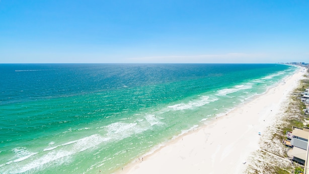 Une plage côtière aux eaux turquoise et limpides, bordée d’un rivage sablonneux.