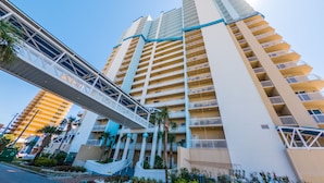 Un hôtel de grande hauteur doté de nombreux balcons, d’un pont piétonnier et d’un espace paysager agrémenté de palmiers.