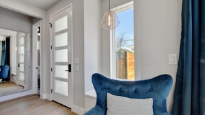 Una sala de estar moderna con un sillón de terciopelo azul, un cojín estampado con motivos geométricos y una lámpara colgante de diseño geométrico.