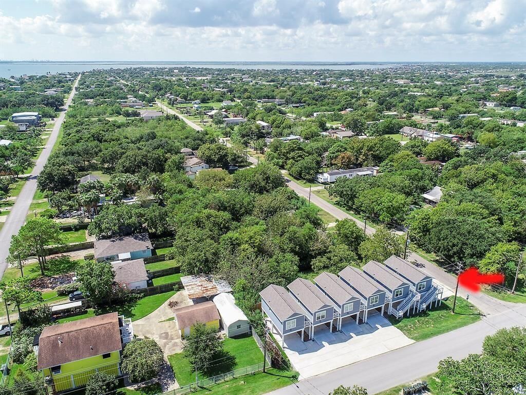 An aerial view of a residential area with houses, a large parking lot, and a body of water in the background.
