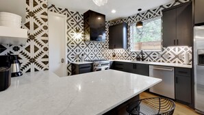 A modern kitchen with a central island, dark cabinets, and patterned backsplash. - InstaWorthy Group Travel Retreat | 3.5 Miles to DT (Austin)