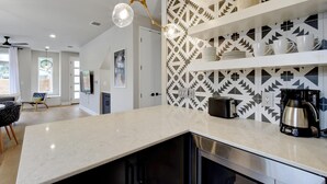 A modern kitchen with a marble countertop, built-in shelves with kitchenware, a coffee maker, and a decorative wall panel. - InstaWorthy Group Travel Retreat | 3.5 Miles to DT (Austin)
