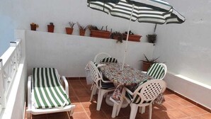 En terrasse med et bord, stole og en stribet liggestol, samt plantekasser på væggen.