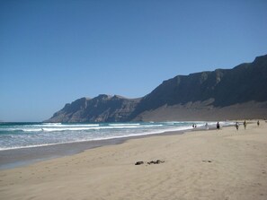 A beach with a rocky cliff in the background and people walking along the shore. - Cozy and spacious apartment 200 meters from the beach (CALETA DE FAMARA)