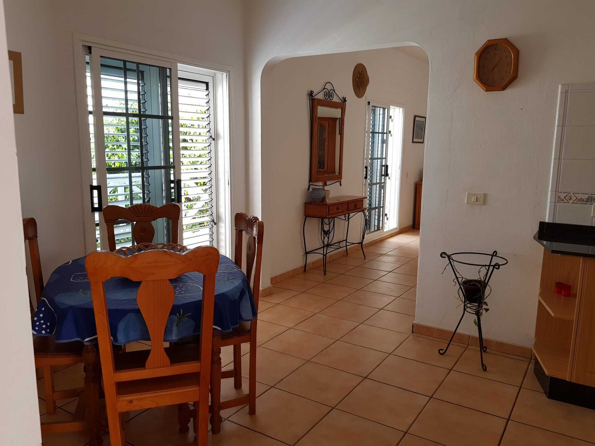 A dining area with a table and chairs, a small table with a mirror, a clock on the wall, and a window with blinds.