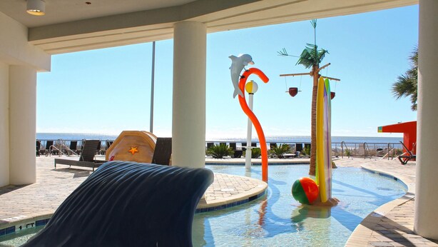 A pool area with a slide, lounge chairs, and a view of the ocean. - Oceans One by Palmetto Vacations (Myrtle Beach)