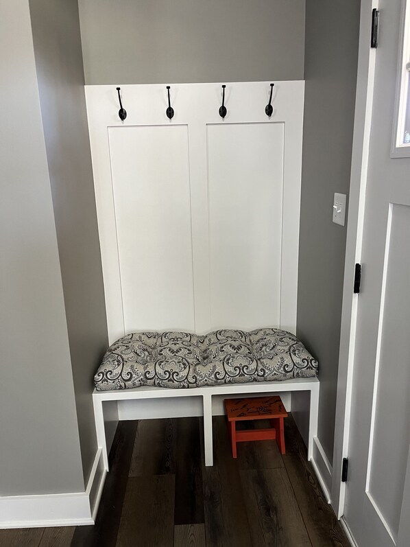 A bench with a patterned cushion, a small stool, and a white wall with three hooks.