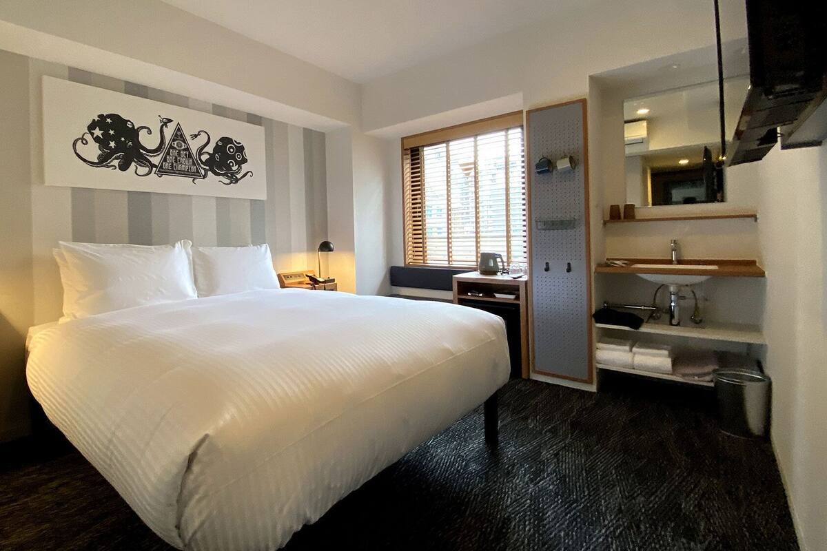 A hotel room with a large bed, a desk with a computer, a mirror, and a wardrobe.