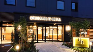 Exterior de l'Hotel Umedaholic, amb entrada ben il·luminada, portes de vidre i zona de jardí ben cuidada.