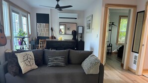 Un salon avec un canapé gris, un ventilateur de plafond et, au fond, un coin repas.