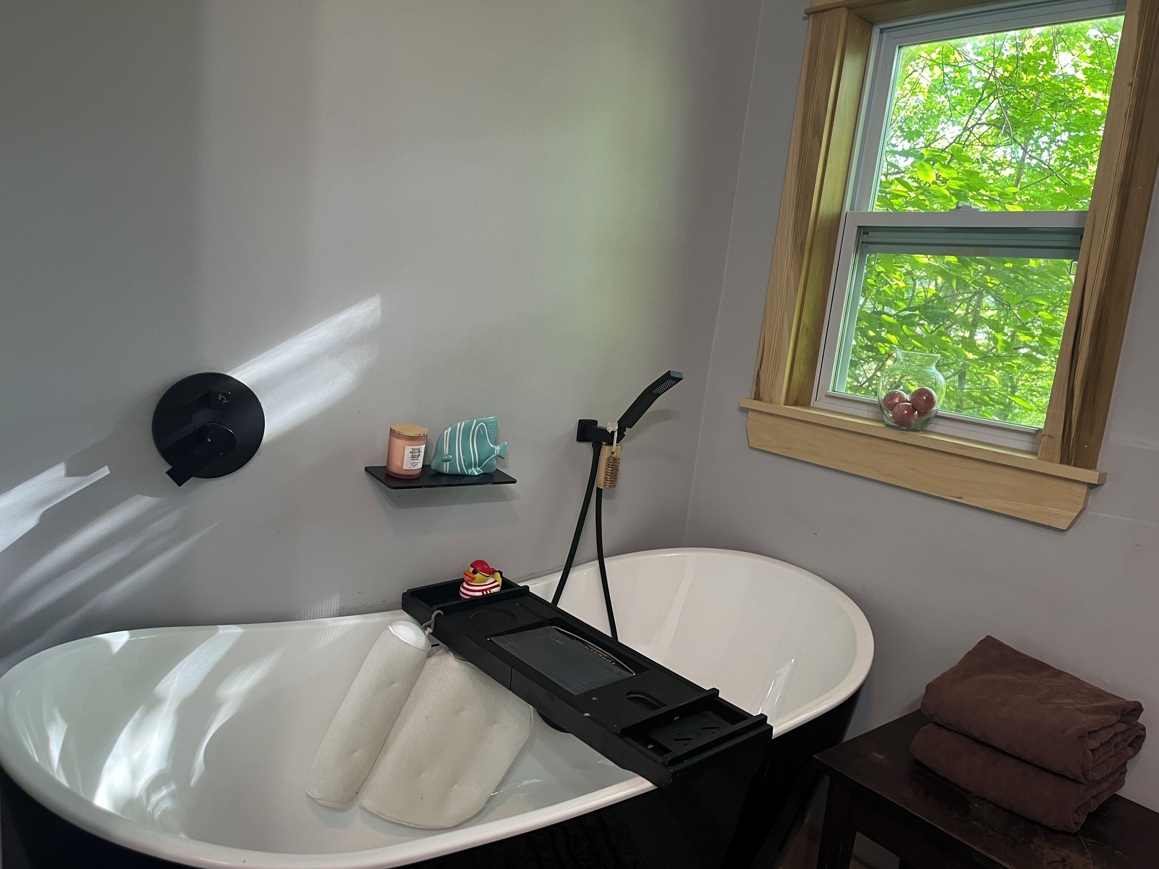 A bathroom with a bathtub, a shelf with toiletries, and a window with a view of trees.
