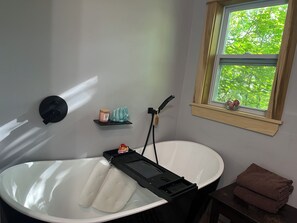 Uma casa de banho com banheira, uma prateleira com artigos de higiene pessoal e uma janela com vista para árvores.