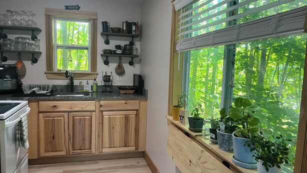 Une cuisine avec des meubles en bois, un plan de travail en granit, une fenêtre avec des stores et une vue sur la verdure à l’extérieur.