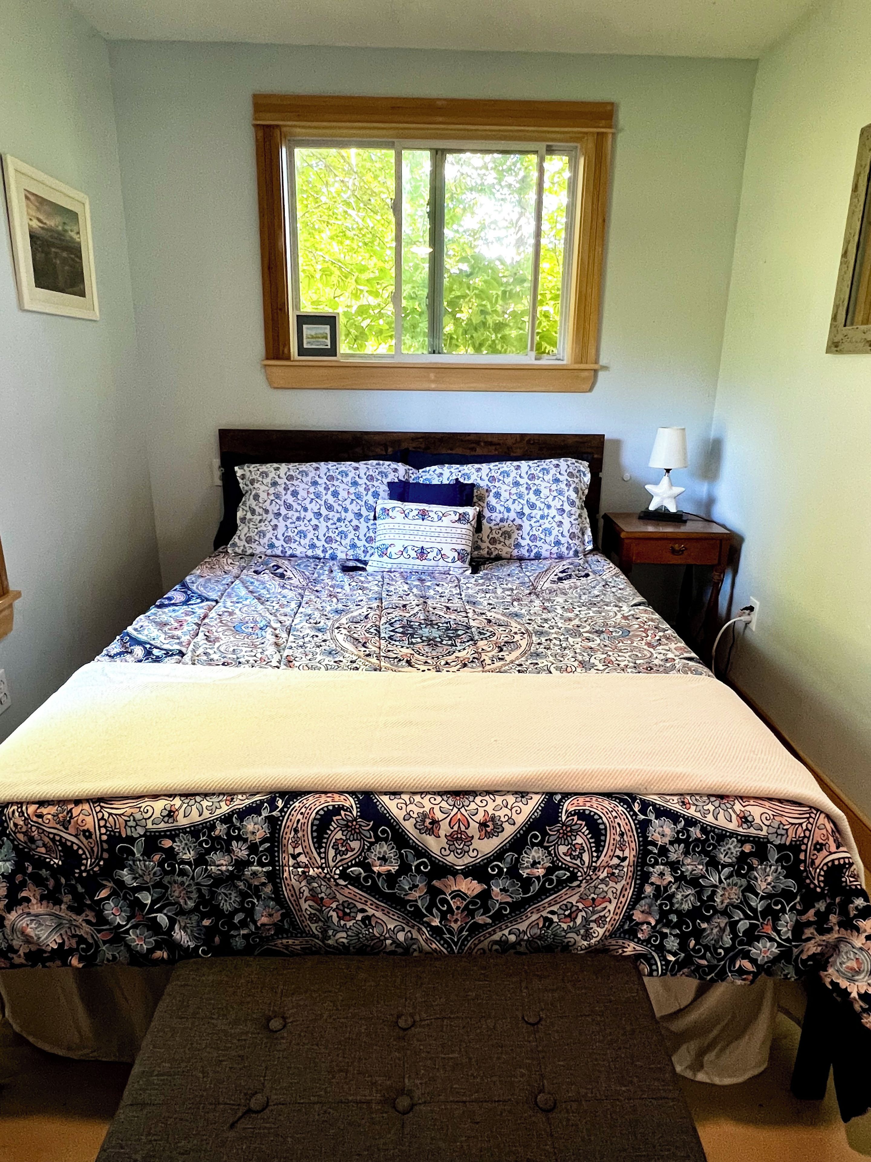 A bedroom with a bed, a window, a nightstand, and a lamp.