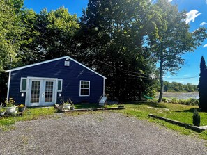 Une maison bleue de plain-pied, dotée d’un porche à l’avant, entourée d’arbres et bordée d’une allée en gravier.