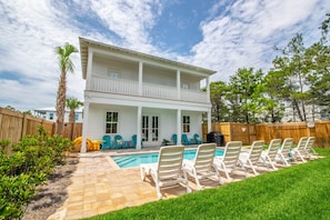 A two-story house with a pool, outdoor chairs, and a wooden fence.