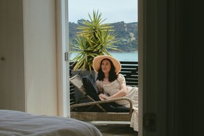 A person seated on a wicker chair with a view of a body of water and hills in the background.