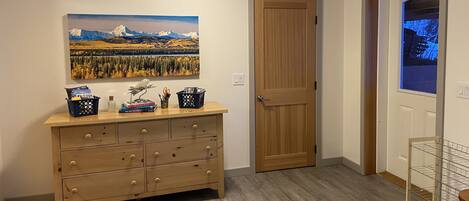 A wooden dresser with drawers, a framed landscape painting, a door, and a window with a view.