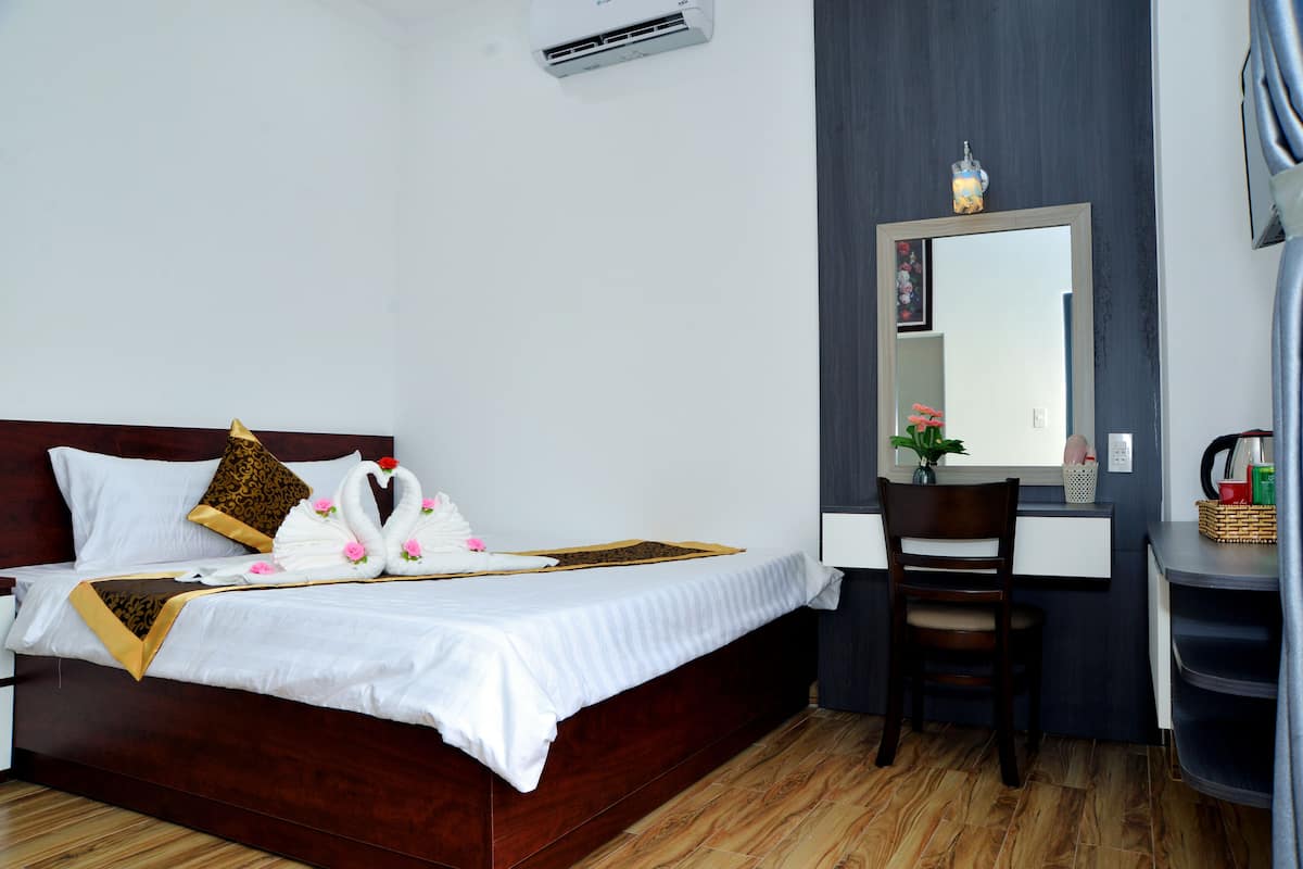 Une chambre d’hôtel avec un lit en bois, un bureau, une chaise et un miroir.
