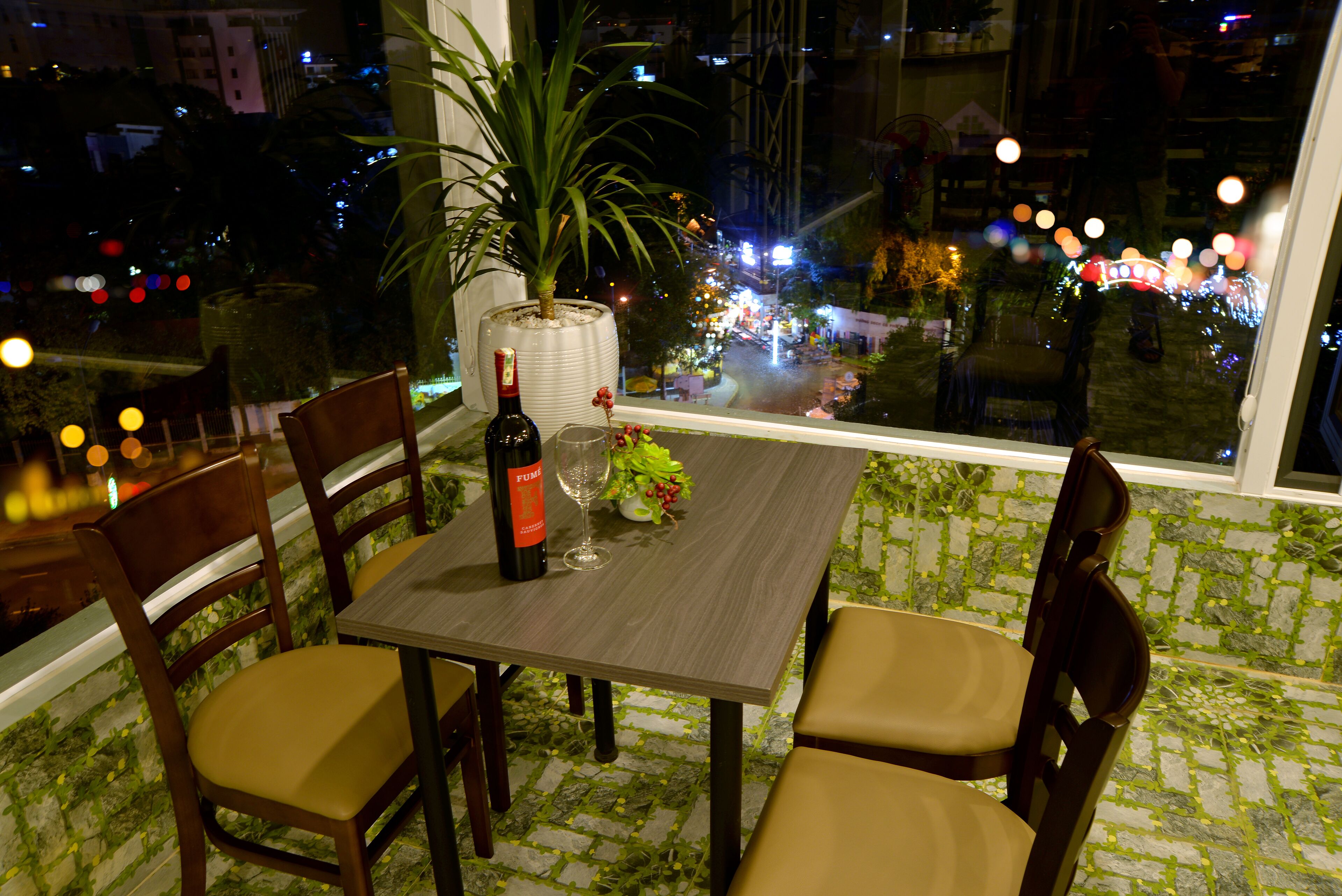 A dining area with a table set for two, a bottle of wine, and a vase with flowers.