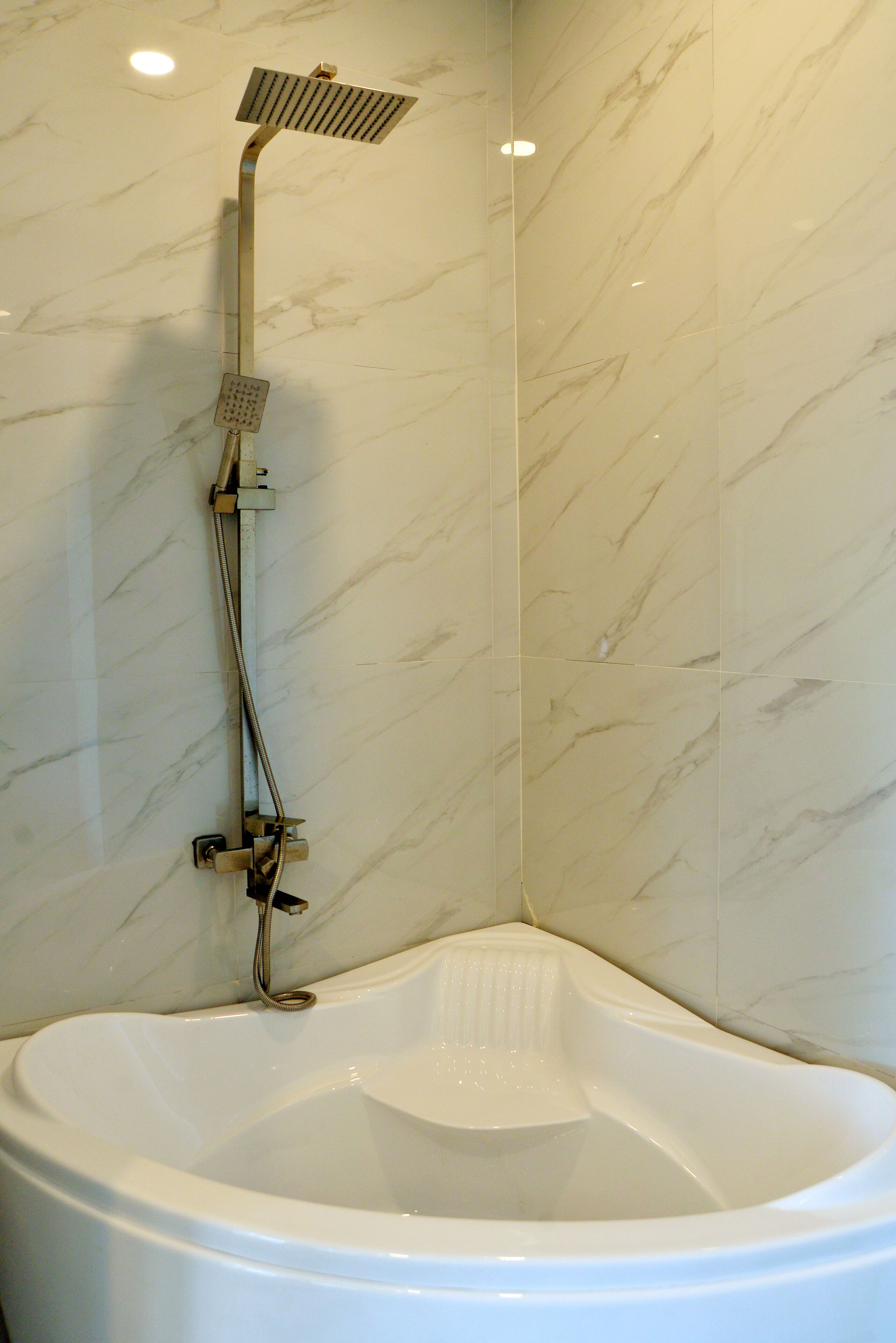 A corner bathroom with a freestanding bathtub, a handheld showerhead, and a wall-mounted faucet.