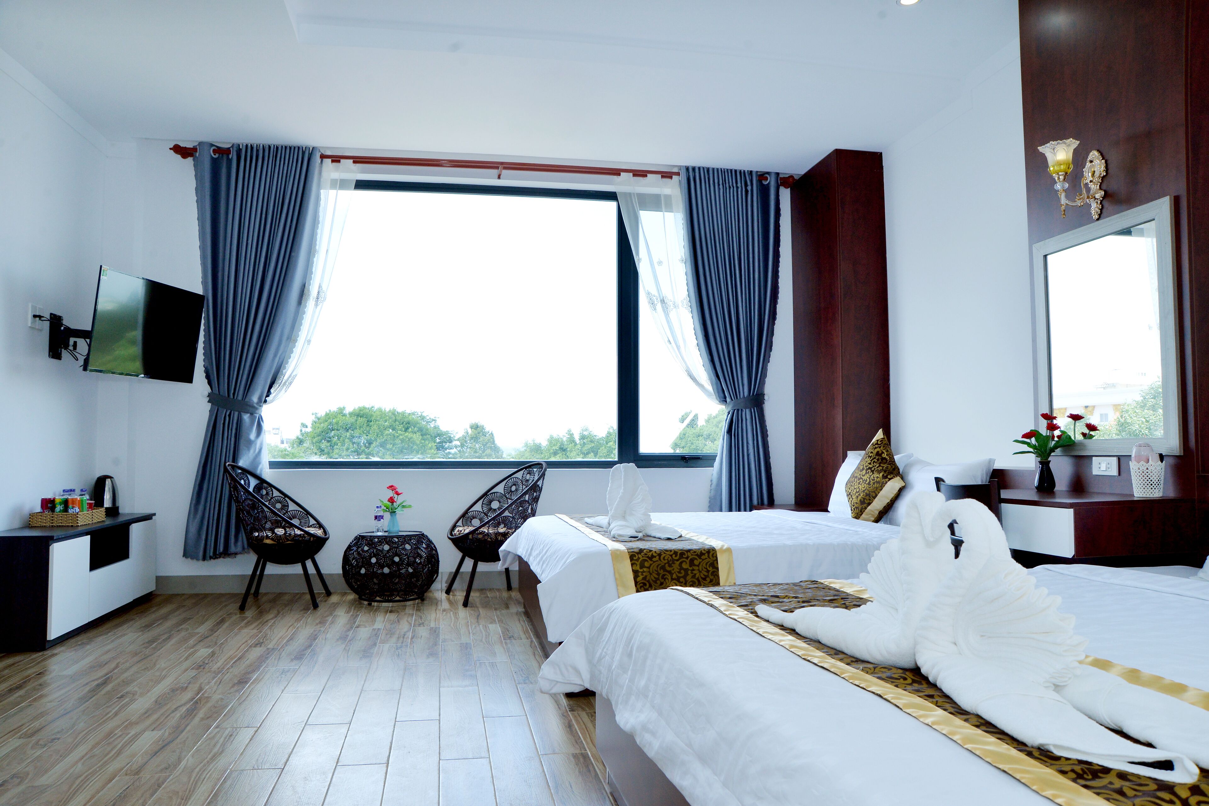 A hotel room with two beds, a TV, a desk with a basket, a chair, and a window with curtains.