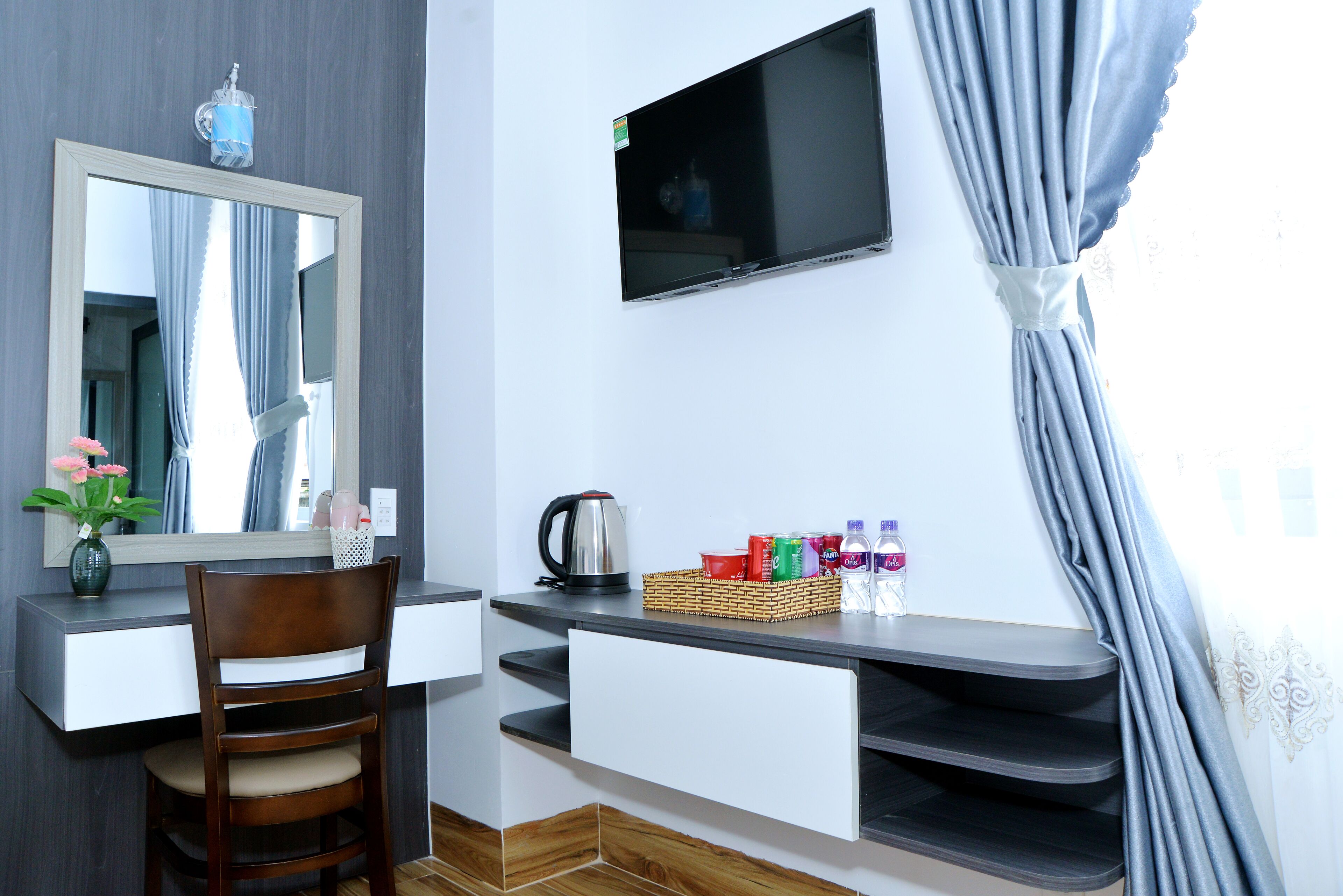 A room with a desk, chair, mirror, TV, and a window with curtains.