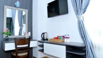 A room with a desk, chair, mirror, TV, and a window with curtains.