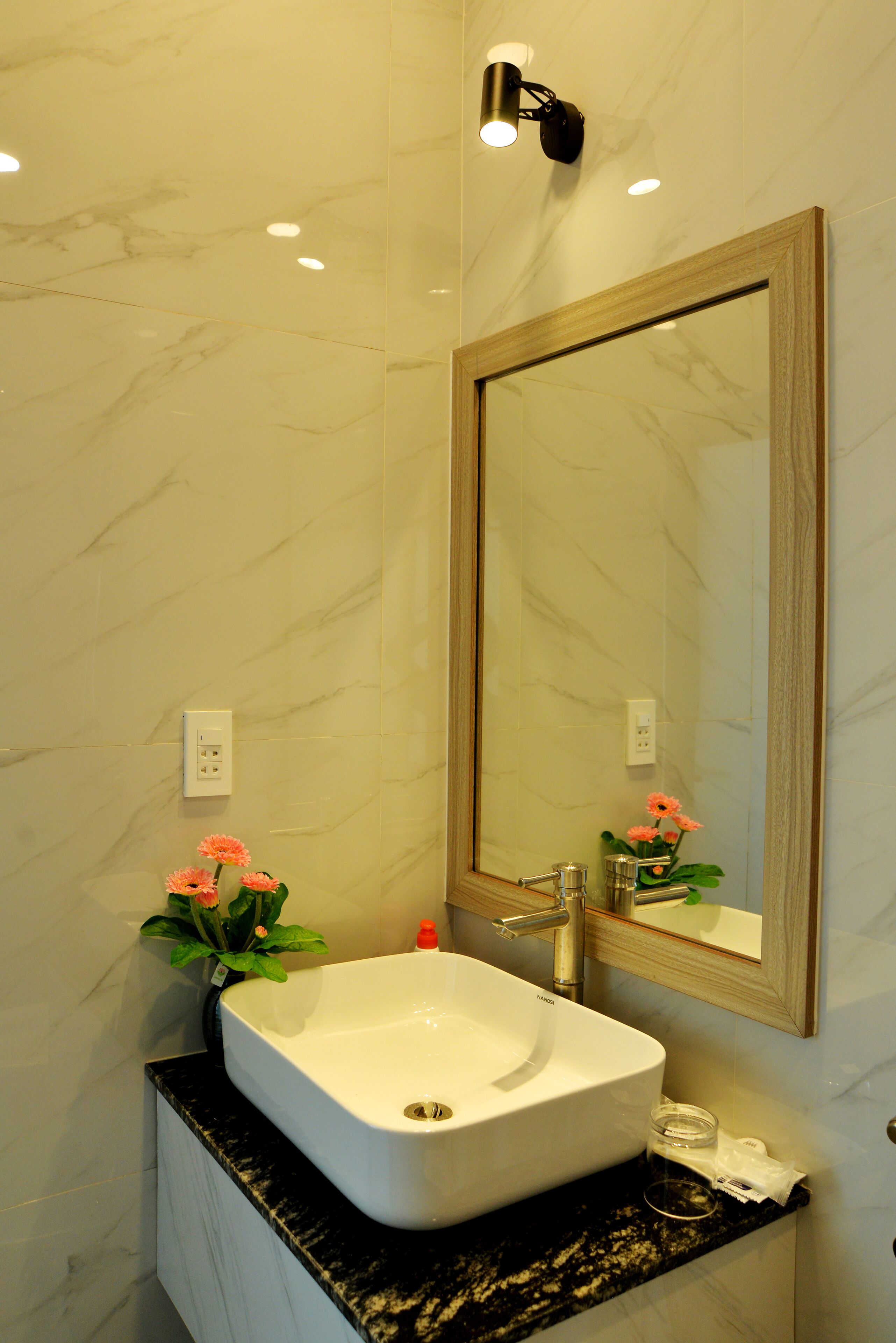 A bathroom with a white marble sink, a large mirror, and a small flower arrangement.