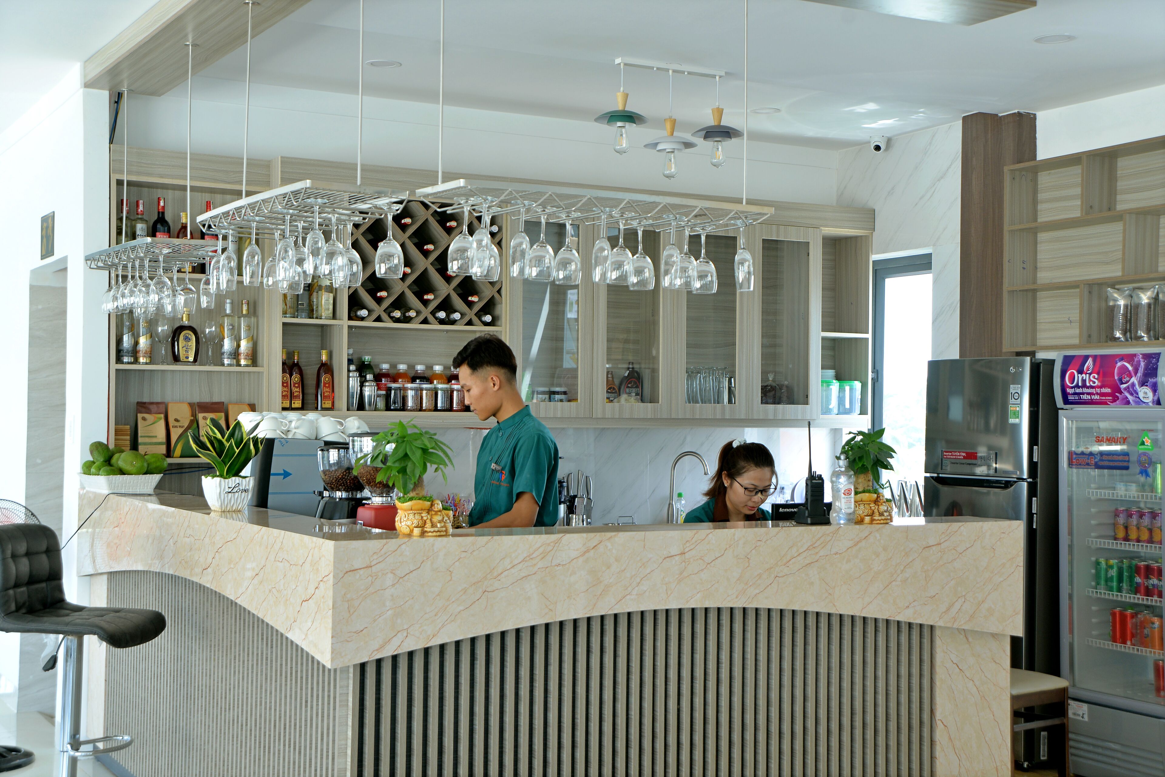 Una zona de bar moderna con mostrador de mármol, copas de vino, botellas y un refrigerador.