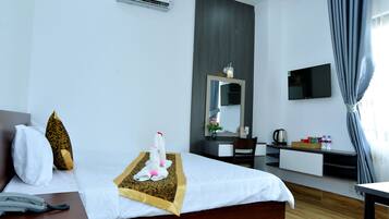 A hotel room with a bed, a desk, a chair, a TV, and a minibar.