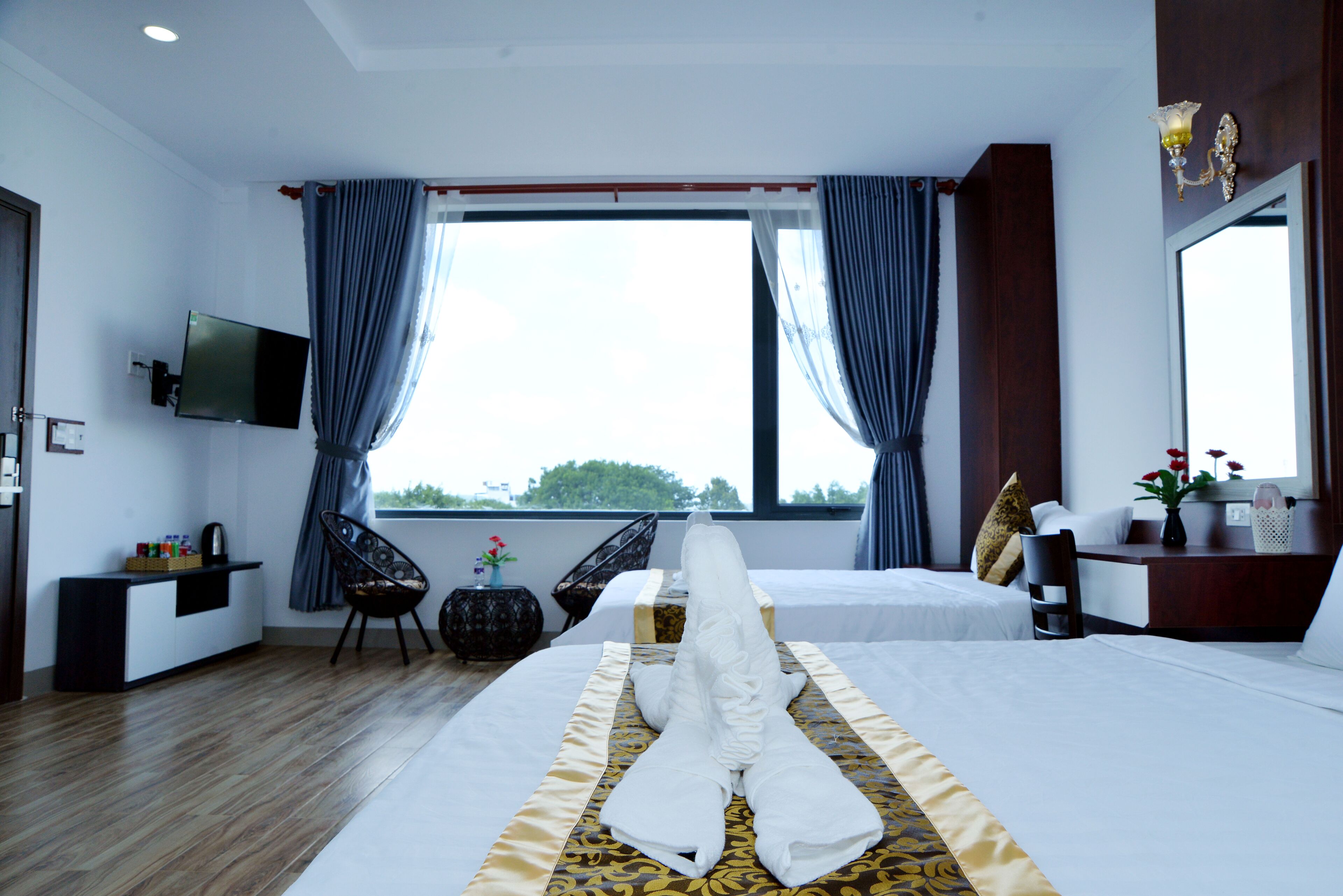 Una habitación de hotel con dos camas, televisión, escritorio y ventana con cortinas.