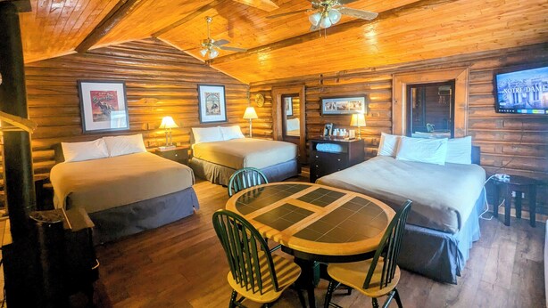 A log cabin-style room with two beds, a dining table, chairs, and ceiling fans. - Teton Court Motel (Pinedale)